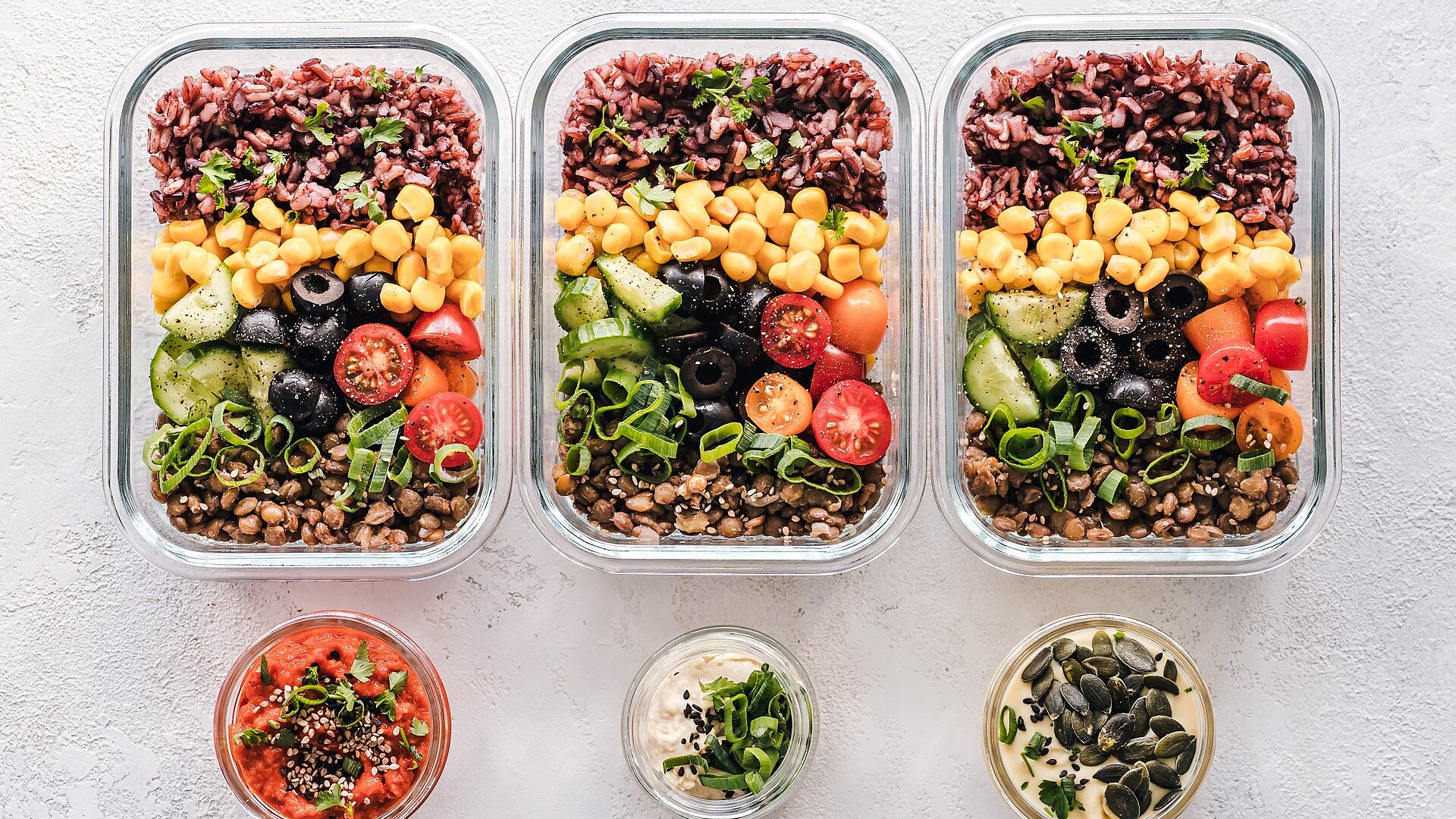 An open lunch box seen from above, five labelled containers side by side on a kitchen counter